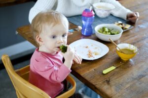 Bebé sentado en su silla comiendo verduras con su familia