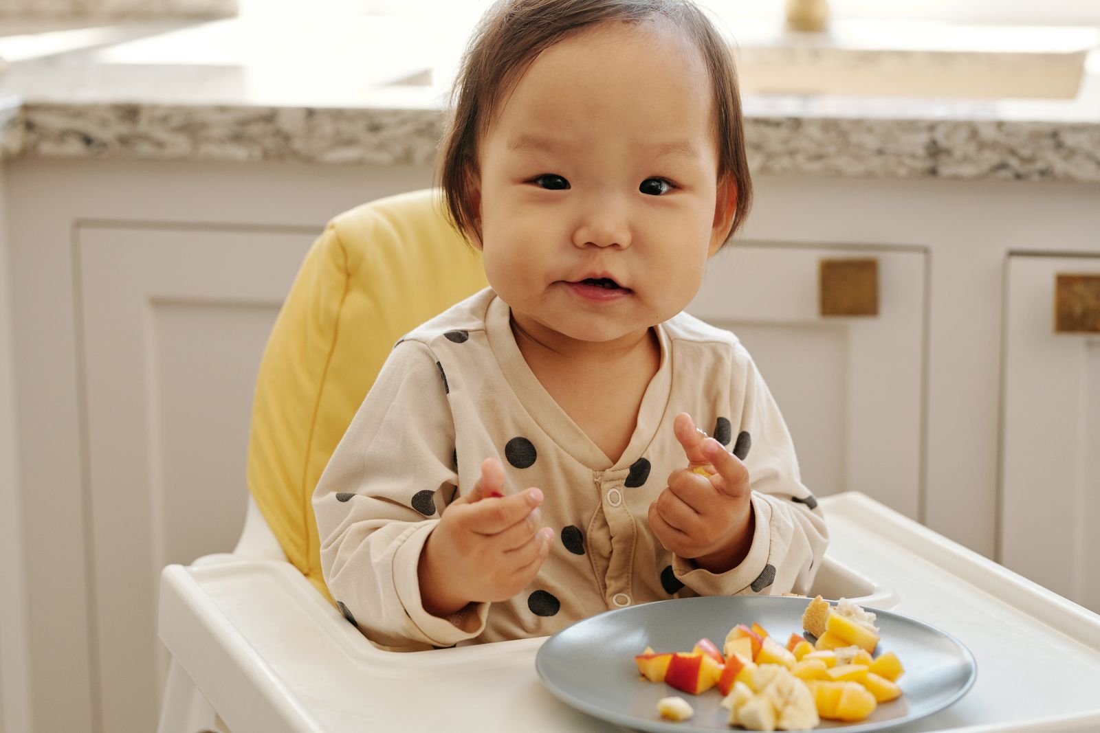 Bebé sentado en su silla comiendo un trozo de alimento con las manos
