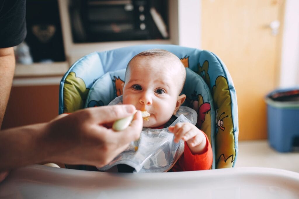 Bebé sentado en su silla comiendo papilla con cuchara